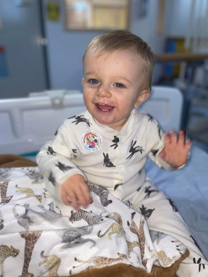 a young child smiling, whilst sat on a hospital bed, wearing cute warm pyjamas.