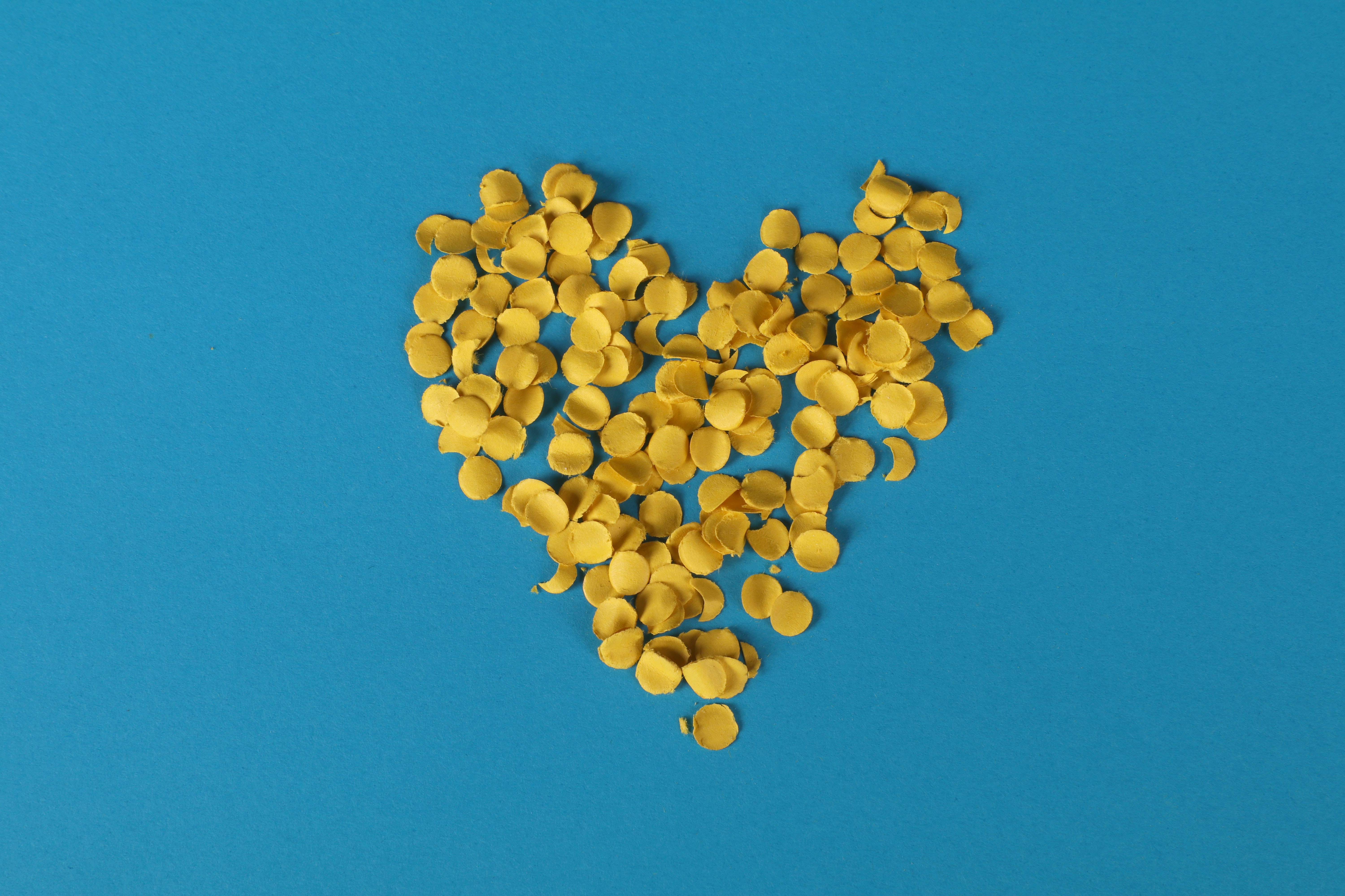 yellow heart made out of confetti on a solid blue background.